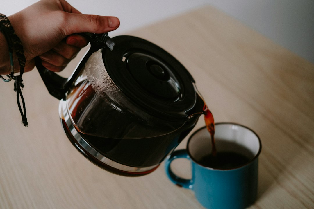 a person pours a cup of coffee into a blue mug